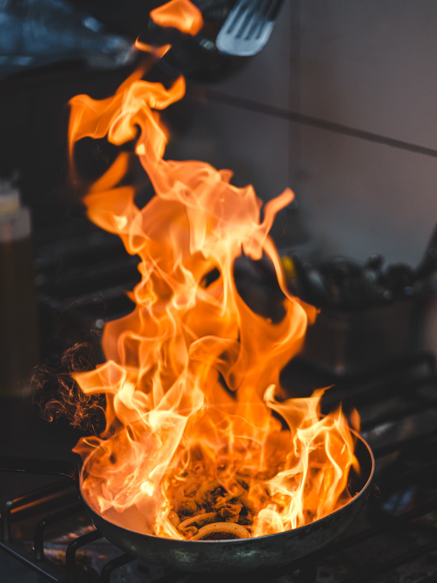 A pan flambé sending a tall column of flame up from the kitchen line.